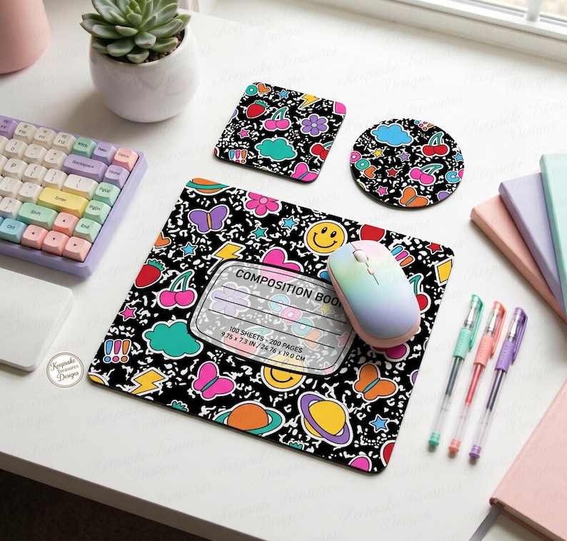 Pu&ograve; includere: Un set di mousepad, sottobicchiere e sottobicchiere quadrato a tema quaderno di composizione nero con grafica colorata di ciliegie, farfalle e faccine sorridenti. Il mousepad misura 24,76 x 19,0 cm. Sono visibili anche un mouse e una tastiera.