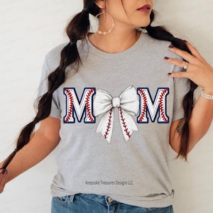 May include: A grey t-shirt with a white bow and the word "MOM" in blue and red baseball stitching.