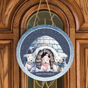 May include: A round, blue and white glitter door hanger with a snowy scene. Three polar bears are standing in front of an igloo. The text "Keepsake Treasures Designs LLC." is at the bottom of the hanger.