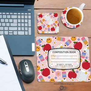 Op de afbeelding: Een roze bureau-opstelling met een laptop, muis en notitieblok. Een muismat, onderzetter en mok in compositieboekstijl hebben een patroon van appels, potloden, smiley-gezichten en bloemen. De muismat is 24,76 x 19,0 cm.