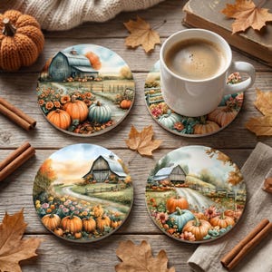 Op de afbeelding: Set van vier keramische onderzetters met een herfstthema. Elke onderzetter heeft een aquarel schilderij van een schuur, pompoenen en bloemen. Een witte mok koffie staat op een onderzetter. Kaneelstokjes en herfstbladeren zijn verspreid.