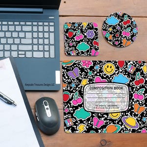 May include: A desk setup featuring a laptop, notebook, and mouse, alongside a composition book, coaster, and square coaster. The composition book and coasters have a black background with colorful illustrations of cherries, clouds, butterflies, and smiley faces. The composition book measures 9.75 x 7.5 inches.