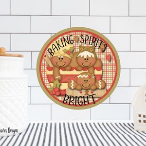 Puede incluir: Señal redonda de madera con fondo de cuadros rojos y blancos. Tres figuras de pan de jengibre sonríen y sostienen utensilios de cocina. El letrero dice "Baking Spirits Bright".