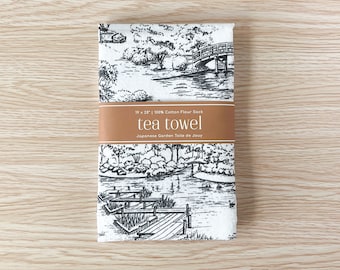 Puede incluir: Toalla de té blanca con una ilustración en blanco y negro de una escena de jardín japonés. El texto "tea towel" y "Japanese Garden Toile de Jouy" está impreso en la toalla. La toalla mide 48 cm por 66 cm.