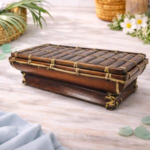 May include: A rectangular wooden box with a bamboo-style lid, secured with woven twine. The box has a rich, dark brown finish, and the lid is made of parallel bamboo pieces. The box is a decorative storage item.