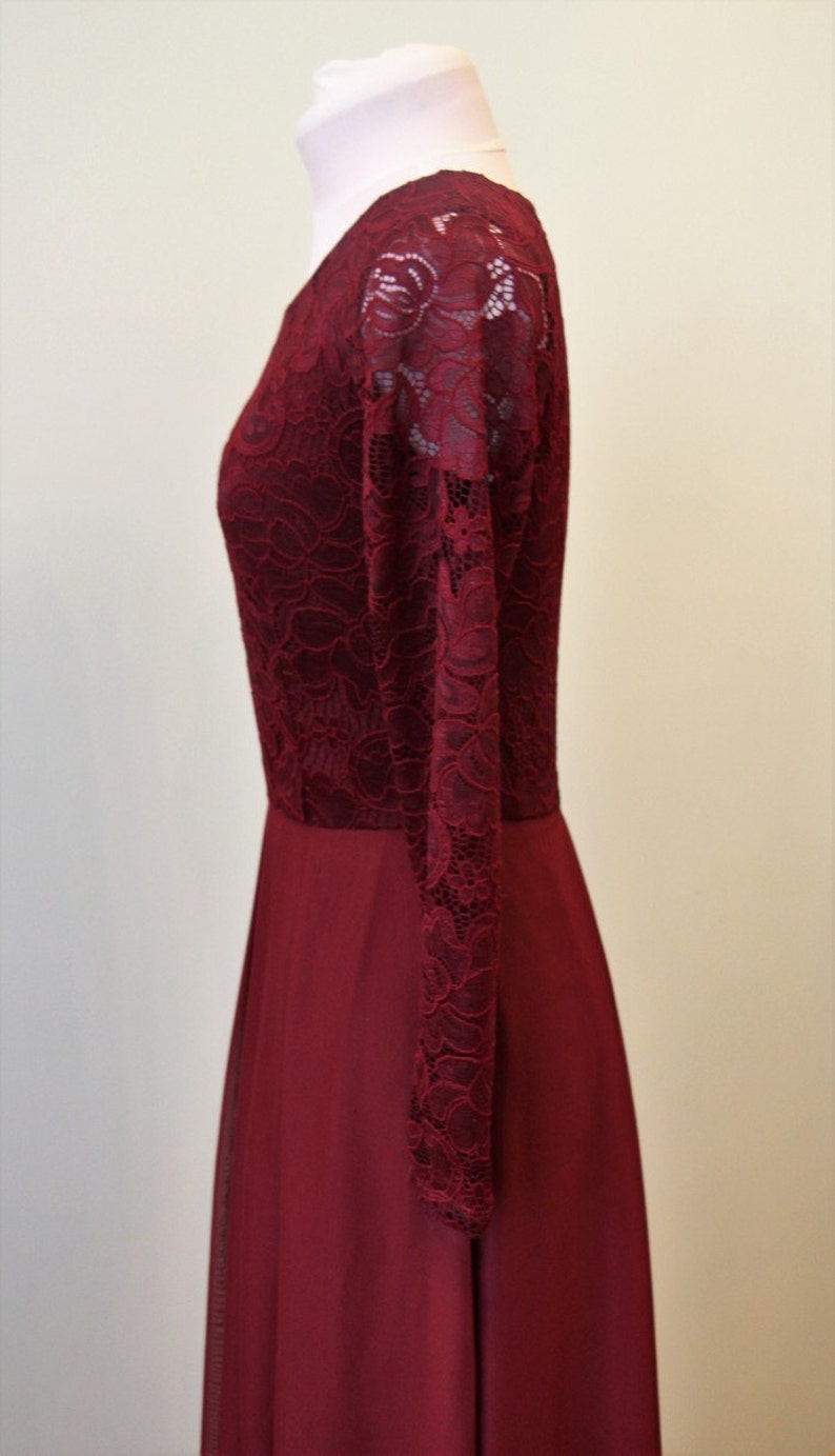 May include: A burgundy maxi dress with long sleeves made of lace. The dress has a fitted bodice and a flowing skirt.