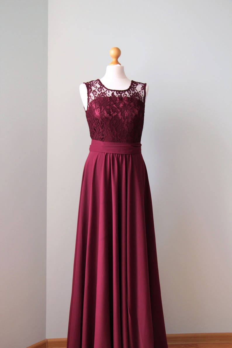 May include: A long, burgundy dress with a lace bodice and a simple, flowing skirt. The dress is sleeveless and has a fitted waist.