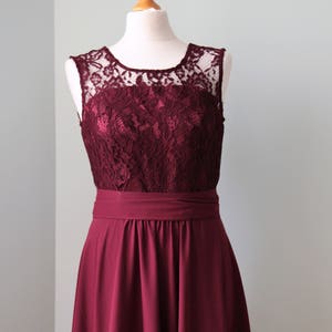 May include: A burgundy sleeveless dress with a lace bodice and a flowing skirt. The dress is on a white mannequin.