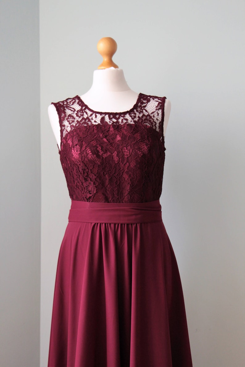 May include: A burgundy sleeveless dress with a lace bodice and a flowing skirt. The dress is on a white mannequin.