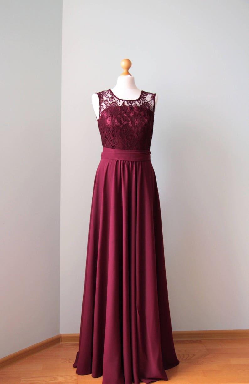 May include: A long, burgundy maxi dress with a lace bodice and a simple, flowing skirt. The dress has a fitted bodice and a wide, satin waistband.