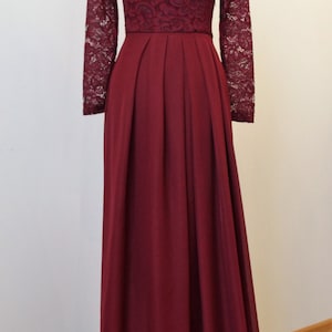 May include: A long, burgundy maxi dress with a lace bodice and long sleeves. The skirt is pleated and flows to the floor.