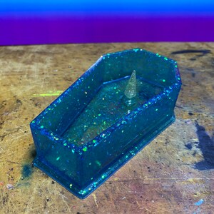 May include: A blue glitter resin coffin-shaped trinket dish with a small silver glitter accent in the center.