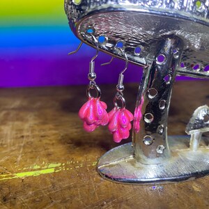 以下が含まれることがあります： ピンクのテクスチャードなバブルのようなデザインのダングルイヤリングのペア。イヤリングはシルバーフックから吊り下げられています。