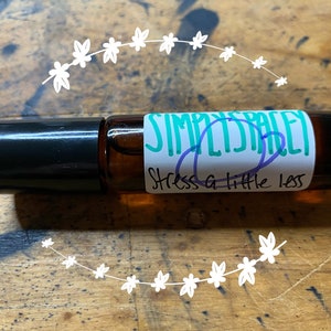 May include: A brown glass roller bottle with a black cap and a white label that says "Simply Spacey Stress a Little Less".