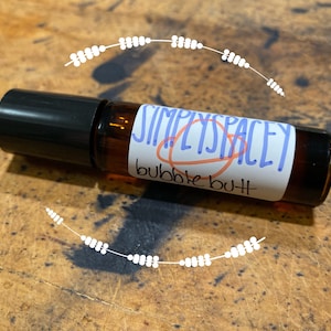 Può includere: Un flacone di vetro marrone con tappo nero e un'etichetta bianca che dice "SIMPLYSPACEY bubble bath".