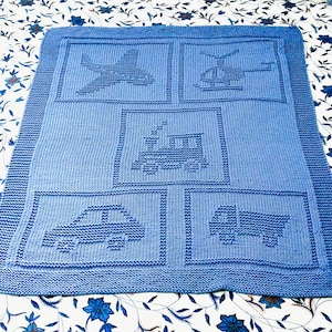 Può includere: Una copertina per neonati di colore blu in maglia con diversi disegni ricamati, tra cui un aereo, un elicottero, un treno, un'auto e un camion.
