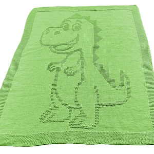 May include: A lime green knitted blanket with a smiling dinosaur design. The blanket features a detailed pattern of the dinosaur's outline, including its head, body, and tail. The edges of the blanket have a ribbed border.