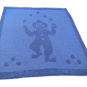 Könnte beinhalten: Eine blaue Strickdecke mit einem Clown-Motiv. Der Clown jongliert mit Bällen, und die Decke hat einen strukturierten Rand. Diese Decke ist ideal für ein Kinderzimmer und ist kuschelig.