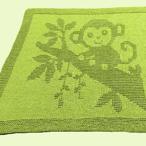 Può includere: Una coperta lavorata a maglia verde lime con un disegno di scimmia. La scimmia è raffigurata su un ramo con foglie. La coperta ha un aspetto strutturato e un bordo pieno.