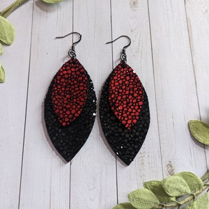 May include: A pair of dangle earrings with black and red leather leaves. The leaves are layered, with the red leaf on top of the black leaf.