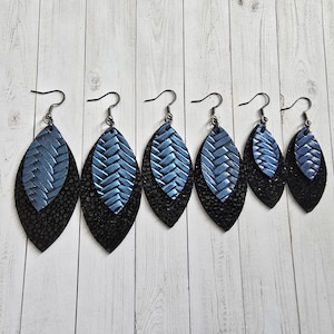 May include: Five pairs of dangle earrings with blue and black leather leaves. The earrings are layered with a blue leaf on top of a black leaf.