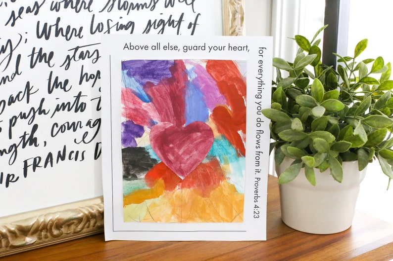 May include: A white card with a colorful painting of a heart surrounded by other hearts. The text "Above all else, guard your heart, for everything you do flows from it. Proverbs 4:23" is printed on the card.