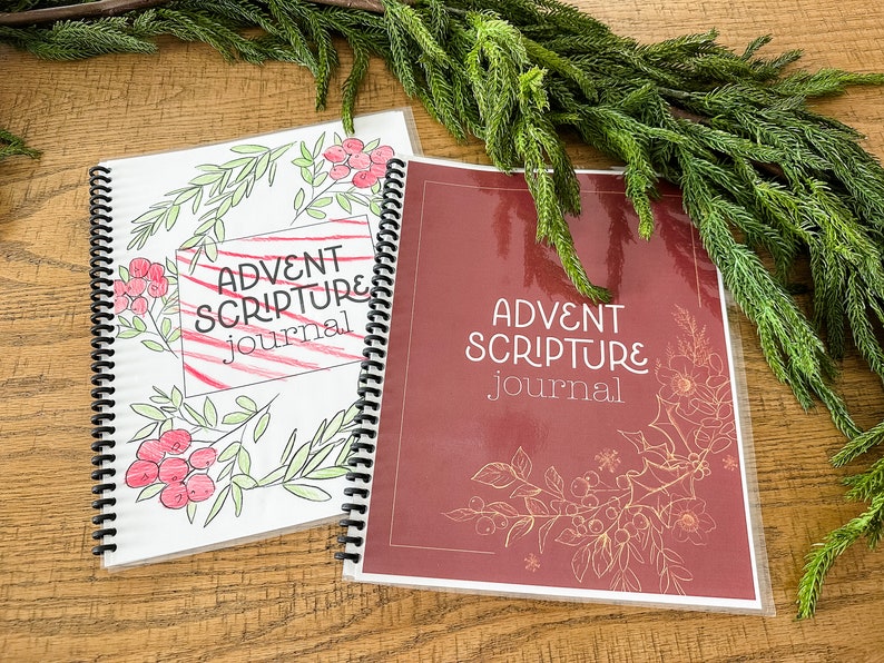 Op de afbeelding: Twee Advent Scripture Journals met een kerstthema. Een journal heeft een witte omslag met rode en groene illustraties en de tekst "Advent Scripture Journal". De andere journal heeft een rode omslag met gouden illustraties en de tekst "Advent Scripture Journal".