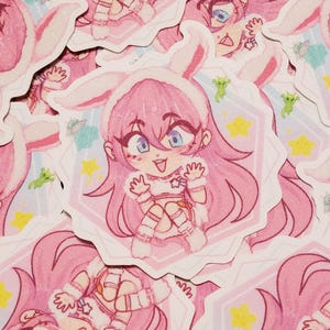May include: Pink stickers featuring a cartoon character with bunny ears, blue eyes, and pink hair. The character is wearing a white outfit with a star on the chest. The stickers have a hexagonal border with stars, aliens, and a spaceship.