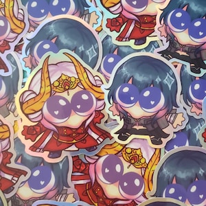 May include: A selection of holographic stickers depicting cartoon characters with oversized eyes. The characters are in red and black attire, with gold details. The stickers have a shimmering, iridescent finish.
