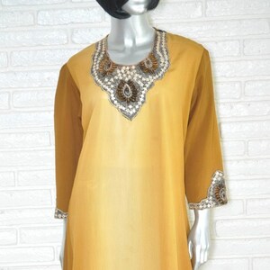 May include: A long, flowing, yellow and brown ombre dress with a beaded neckline and beaded trim on the sleeves.