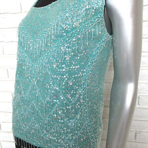 May include: A sleeveless turquoise sequined top with a beaded fringe trim. The top is made of a sheer fabric and has a scoop neckline.