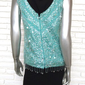 May include: A sleeveless turquoise sequined vest with a zipper down the back and a fringe trim. The vest is worn over a black top.