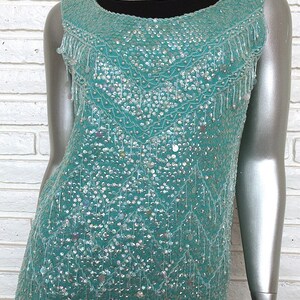 May include: A sleeveless turquoise top with a sequined design and fringe trim. The top is made of a soft, lightweight fabric and has a relaxed fit.