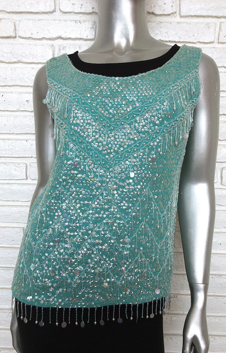 May include: A sleeveless turquoise top with a sequined design and fringe trim. The top is made of a soft, lightweight fabric and has a relaxed fit.