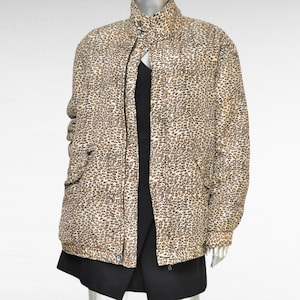 Puede incluir: Una chaqueta de color marrón y blanco con estampado de leopardo y cierre de cremallera. La chaqueta tiene un cuello alto y dos bolsillos.