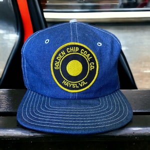 May include: A blue denim baseball cap with a curved peak. The cap has a circular patch with the text "GOLDEN CHIP COAL CO. HAYSI, VA." in yellow and black. The cap has a light blue top button and eyelets.