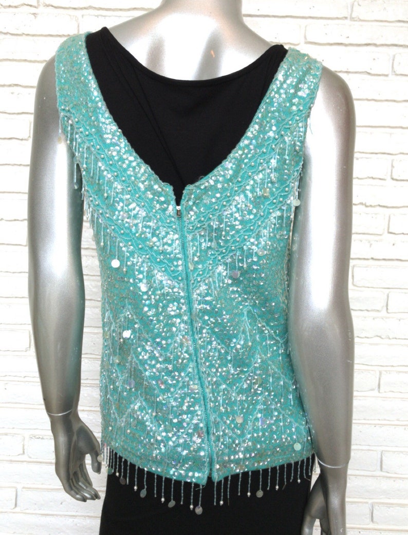 May include: A sleeveless turquoise sequined top with a zipper down the back and a fringe trim.