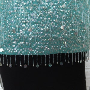 May include: A teal blue sequined top with a fringe trim. The sequins are iridescent and create a shimmering effect.