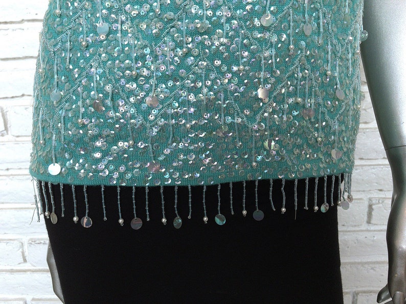 May include: A teal blue sequined top with a fringe trim. The sequins are iridescent and create a shimmering effect.