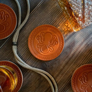 May include: Four brown leather coasters with an embossed octopus design. The coasters are round and have a rope border.