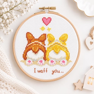 Puede incluir: Un bastidor de bordado circular de madera con un patrón de punto de cruz de la parte trasera de dos perros, uno marrón y otro amarillo, con almohadillas rosas. Sobre los perros hay un corazón rosa y dos estrellas amarillas. Texto "I waff you.."