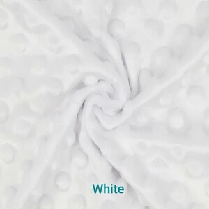 May include: White fabric with a textured, dimpled surface. The fabric is soft and plush, with a swirling pattern. The word "White" is printed in the image. This fabric is suitable for blankets, baby items, and other craft projects.