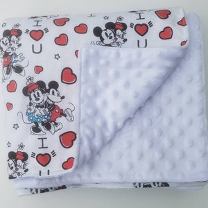 May include: White baby blanket featuring a pattern of Mickey and Minnie Mouse, red hearts, and the text "I ❤️ U." The blanket has a soft, textured white underside. The blanket is folded, showing both the patterned top and the plush underside.