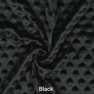 May include: Black minky fabric with a raised dot pattern. The plush material is soft and textured, with a slight sheen. The word "Black" is printed in white text on the fabric. This fabric is suitable for various sewing projects.