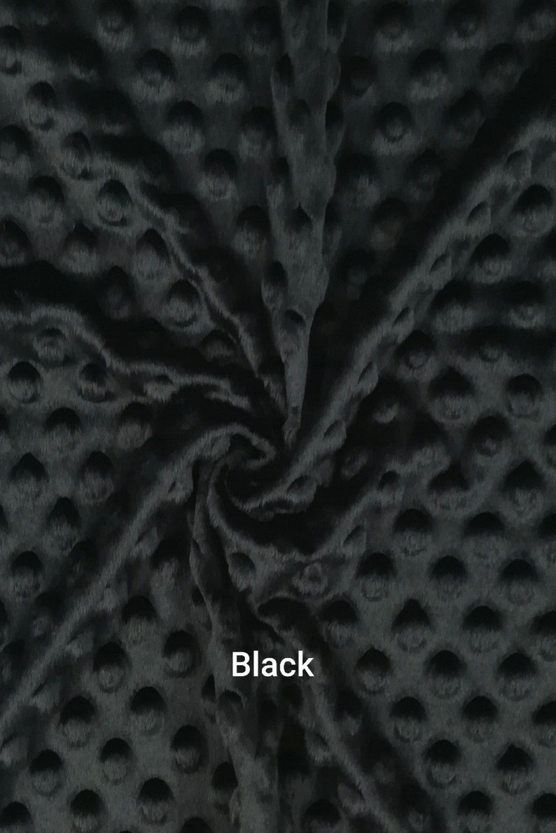 May include: Black minky fabric with a raised dot pattern. The plush material is soft and textured, with a slight sheen. The word "Black" is printed in white text on the fabric. This fabric is suitable for various sewing projects.