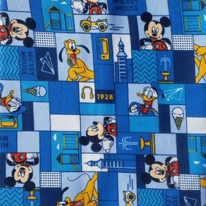 Puede incluir: Una tela azul y blanca con un patrón repetido de Mickey Mouse, Donald Duck y Goofy. El patrón también incluye imágenes de una ciudad, una fuente y un avión de papel. El texto "Mickey Mouse" y "1928" también están incluidos en el patrón.