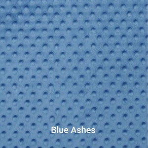 May include: Close-up of a blue fabric with a textured, dimpled surface. The fabric is a solid color, with the text "Blue Ashes" printed on it. A ruler is at the bottom, showing measurements in inches.