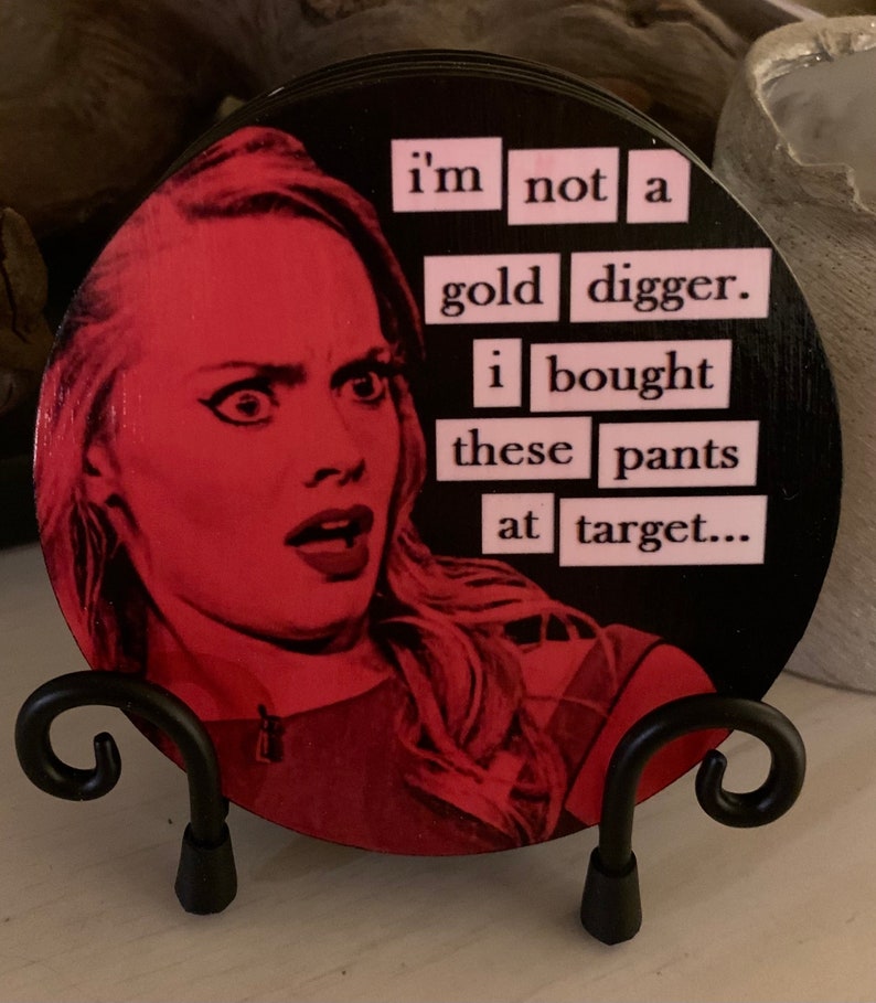 May include: A round coaster with a black background and a pink and white image of a woman with the text "i'm not a gold digger. i bought these pants at target..." printed on it.
