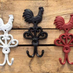 May include: Three cast iron rooster hooks in white, black, and red. Each hook features a rooster design with a double hook at the bottom.