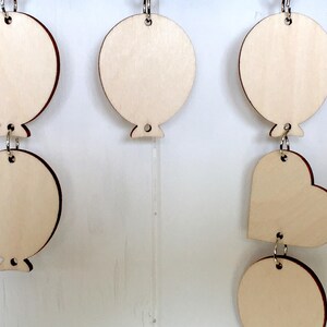Puede incluir: Una guirnalda de madera con una cadena de adornos redondos y en forma de coraz&oacute;n. Los adornos est&aacute;n sin terminar y listos para ser pintados o decorados.